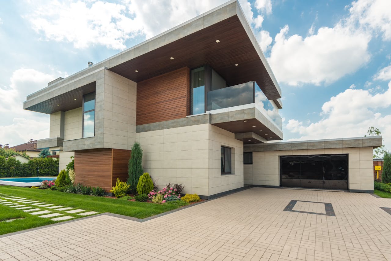 services-05 Contemporary luxury house with a sleek design, lush garden, and blue sky.